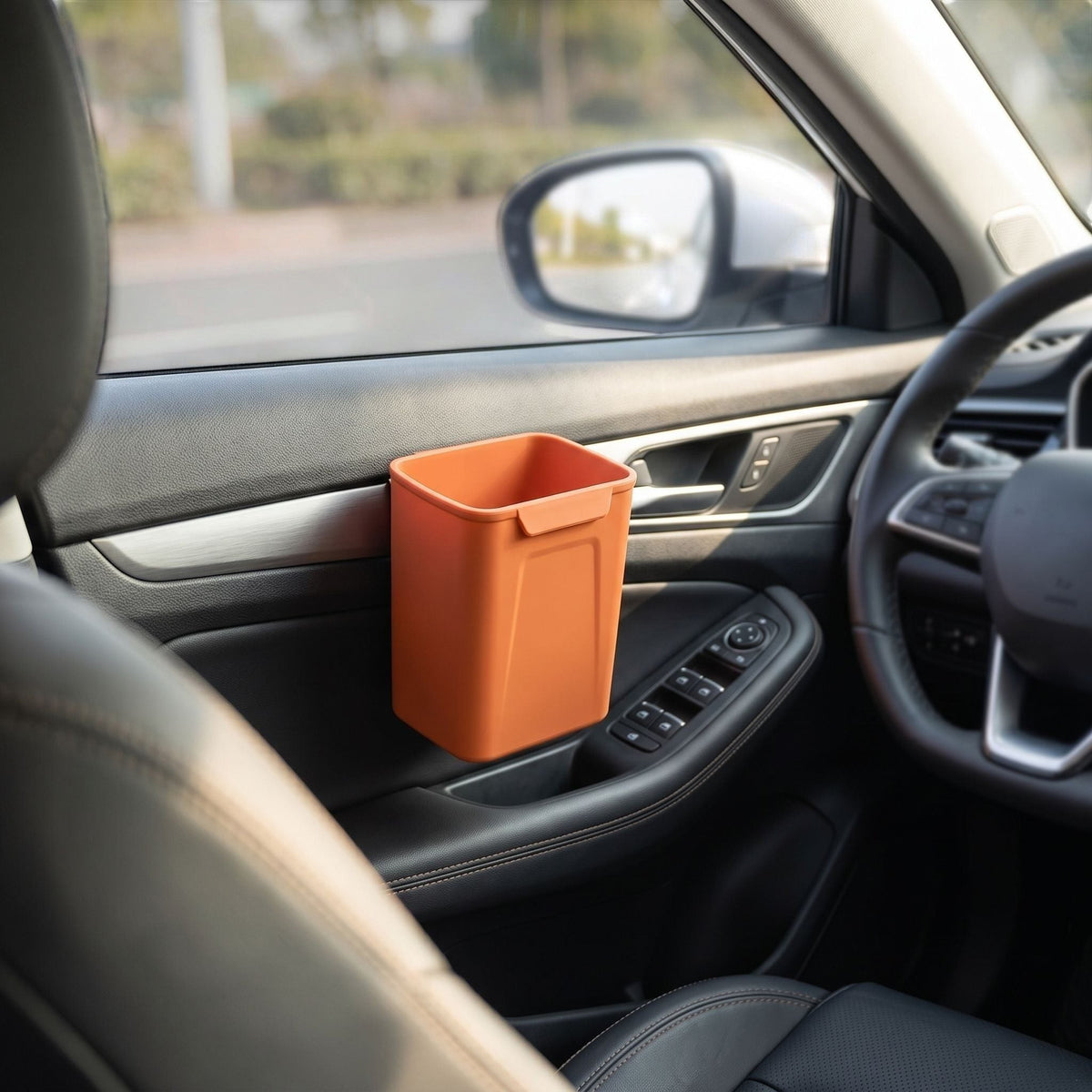 Silicone car trash bin clipped on the door of a vehicle in an outdoor environment, illuminated by sunlight to show its size and utility in real-world use.