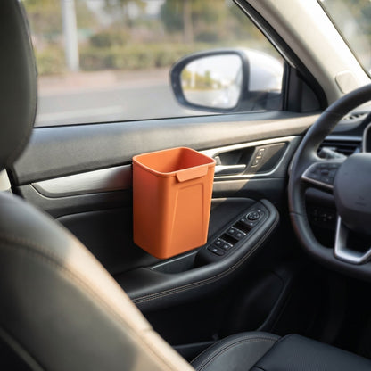 Silicone car trash bin clipped on the door of a vehicle in an outdoor environment, illuminated by sunlight to show its size and utility in real-world use.