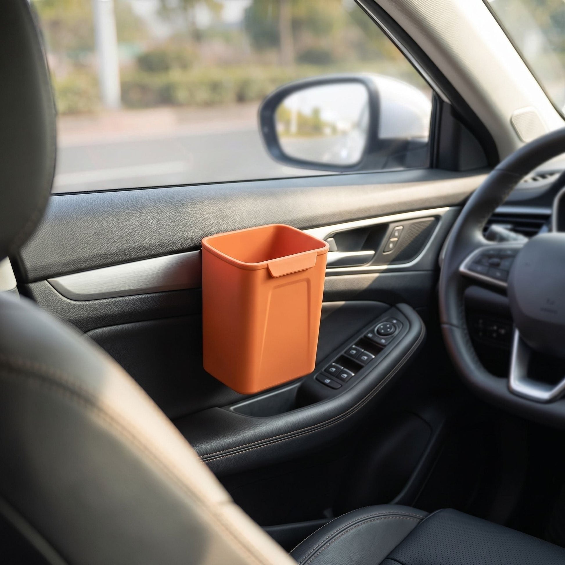 Silicone car trash bin clipped on the door of a vehicle in an outdoor environment, illuminated by sunlight to show its size and utility in real-world use.