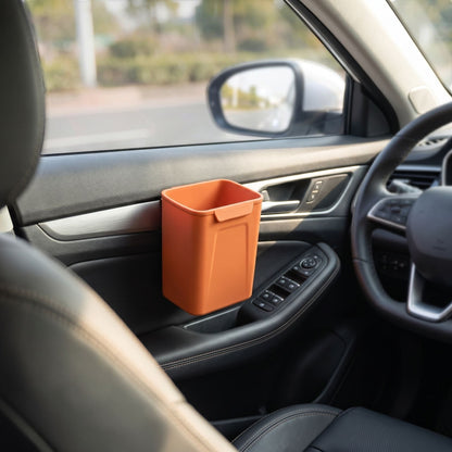 Silicone car trash bin clipped on the door of a vehicle in an outdoor environment, illuminated by sunlight to show its size and utility in real-world use.