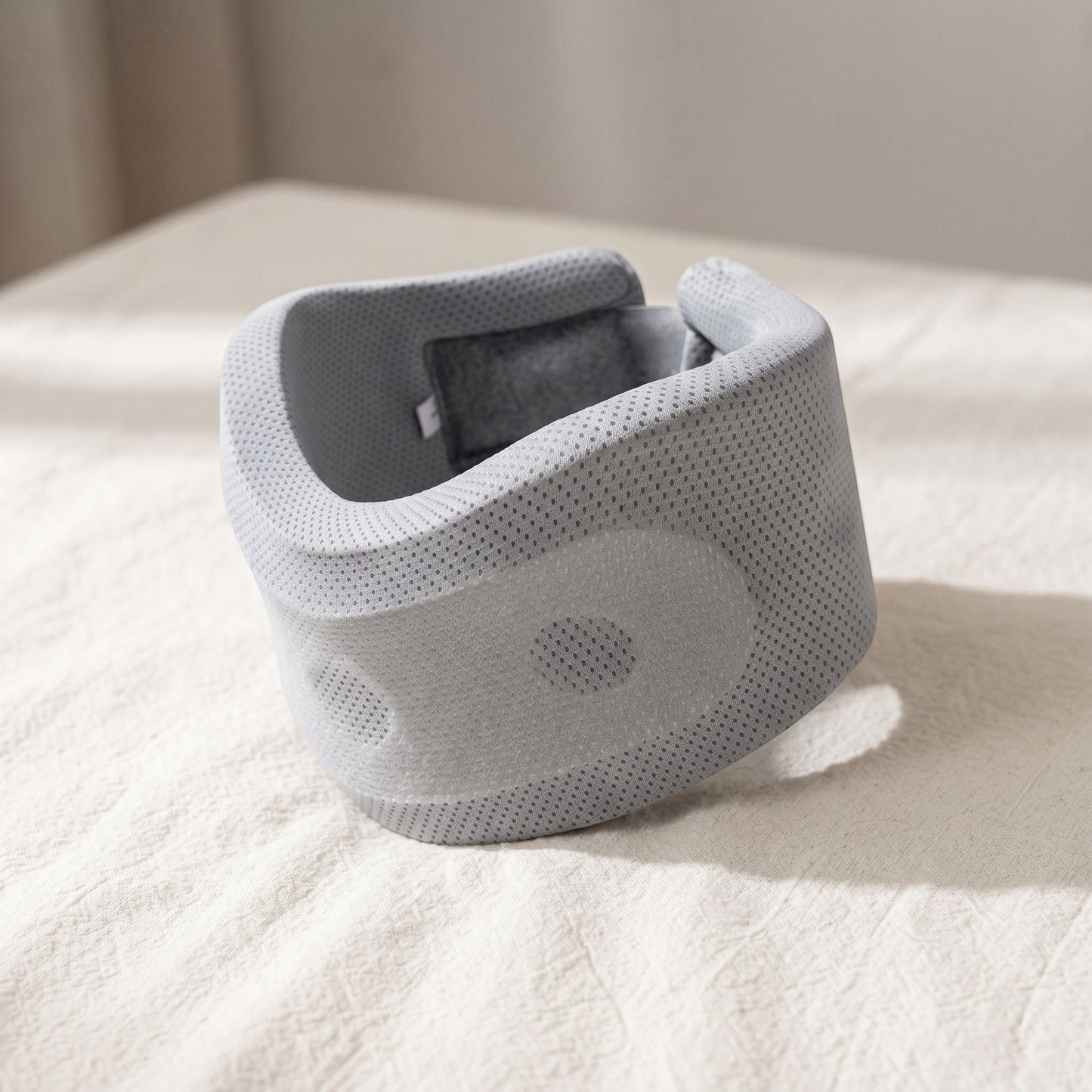 Close-up of small unbranded neck support pillow highlighting non-woven fabric and contoured form with soft directional lighting.