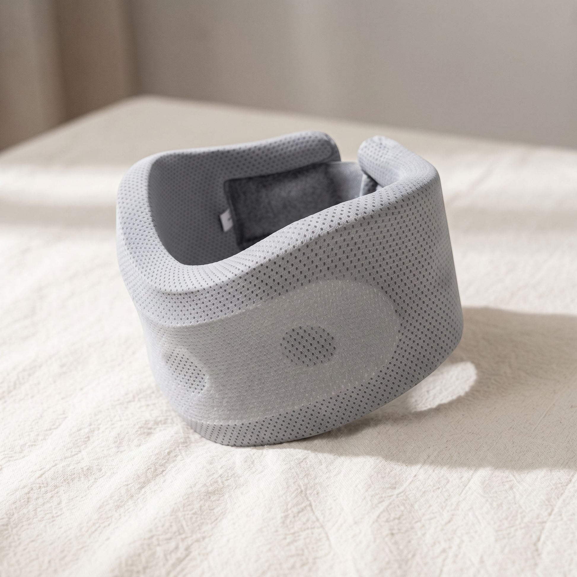 Close-up of small unbranded neck support pillow highlighting non-woven fabric and contoured form with soft directional lighting.