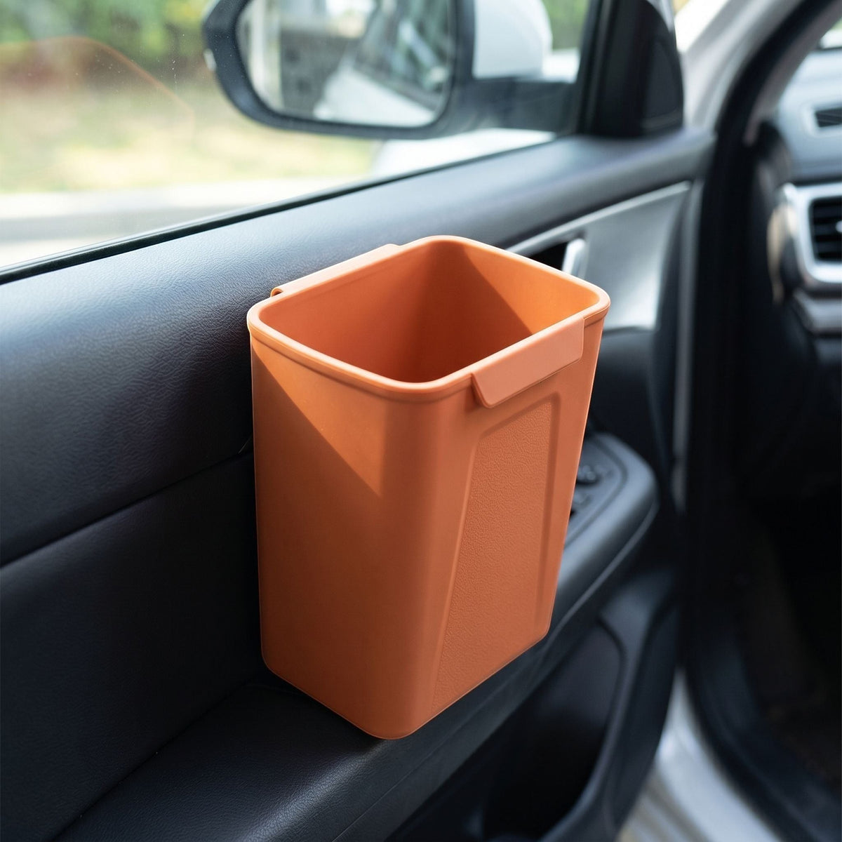 Detailed view of a silicone car trash bin attached to a car door, highlighting the clip mechanism and textured waterproof silicone surface under natural daylight.