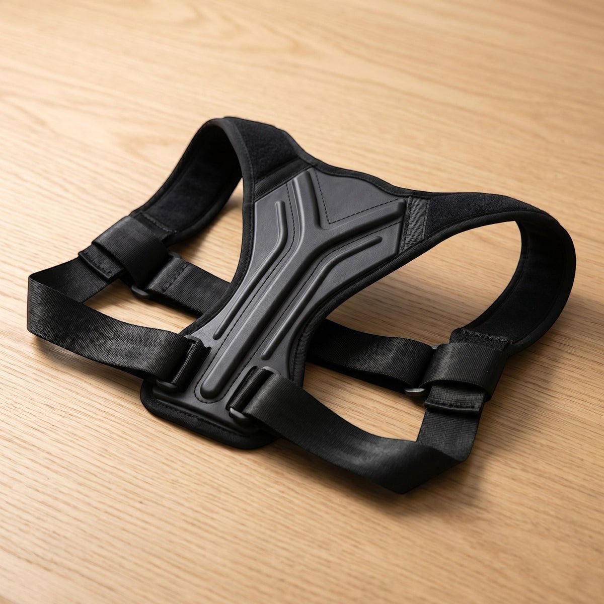Close-up of unbranded posture brace showing textured material and adjustable straps on a light wooden surface with natural side lighting.