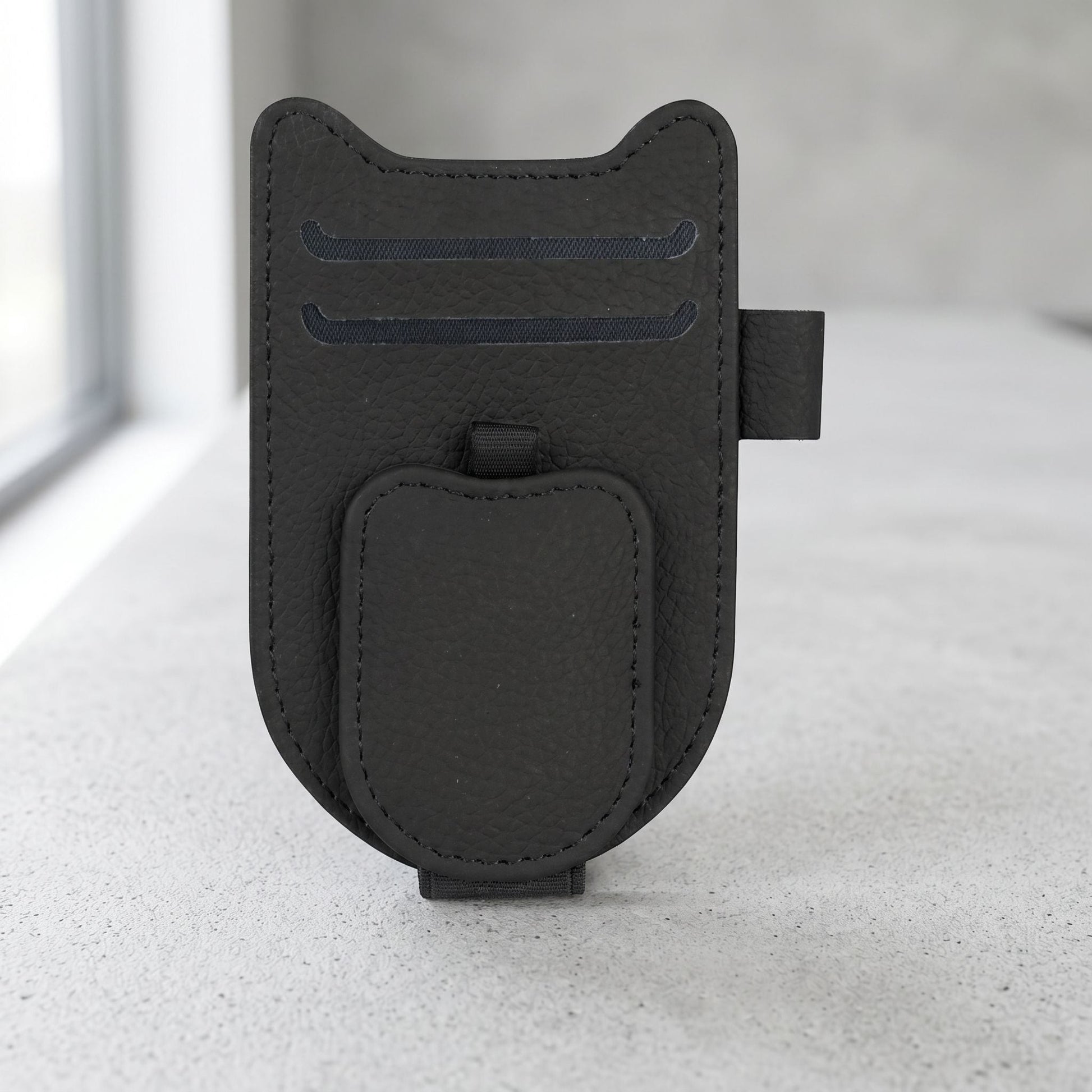 Clean product photo of magnetic car sunglasses holder clip with leatherette finish, centered on neutral surface in well-lit studio.