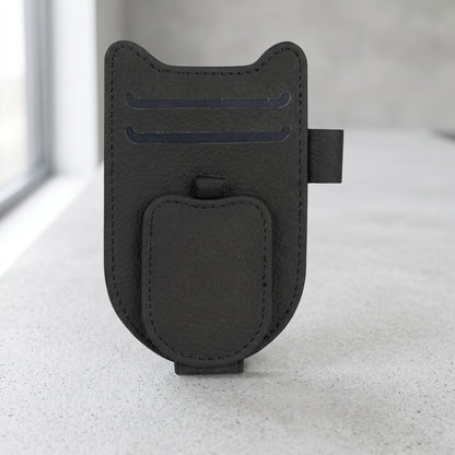 Clean product photo of magnetic car sunglasses holder clip with leatherette finish, centered on neutral surface in well-lit studio.