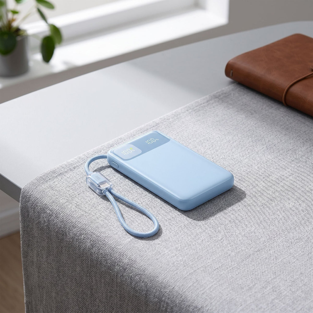 Modern workspace scene with a small power bank displaying battery status and dual USB-C cables on a textured surface.