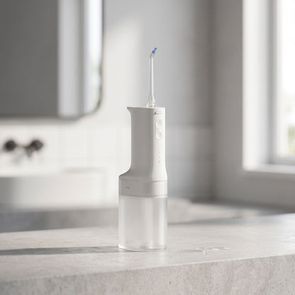 Side view of a small electric water flosser focusing on its slim profile and water tank, with a blurred bathroom background for context.