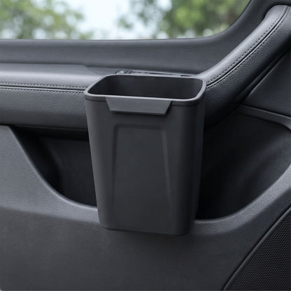 Unbranded silicone car trash bin clipped onto a vehicle door panel, showcasing its compact design and waterproof silicone surface in a realistic car interior setting.