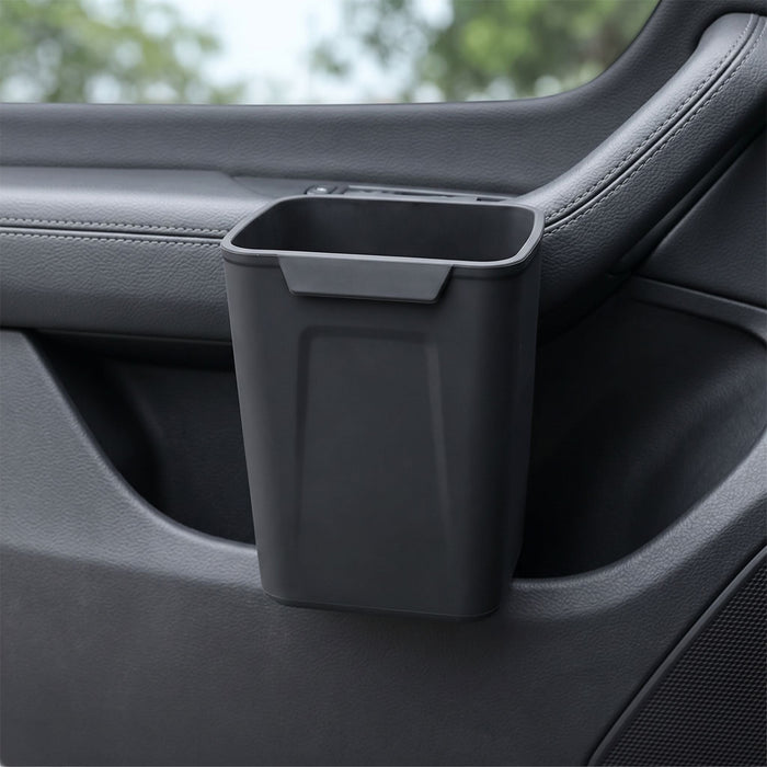 Unbranded silicone car trash bin clipped onto a vehicle door panel, showcasing its compact design and waterproof silicone surface in a realistic car interior setting.