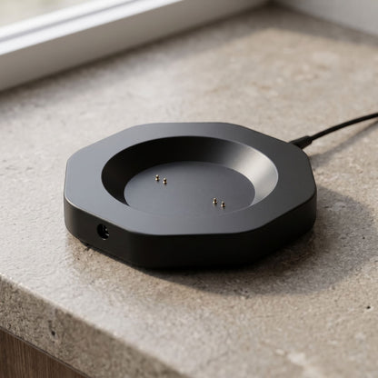 Close-up of a black smart mug charging dock with probe interface on a neutral textured surface, highlighting its compact design and matte finish.