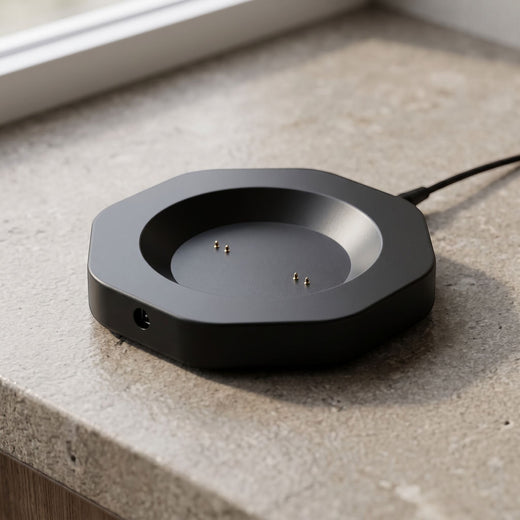 Close-up of a black smart mug charging dock with probe interface on a neutral textured surface, highlighting its compact design and matte finish.