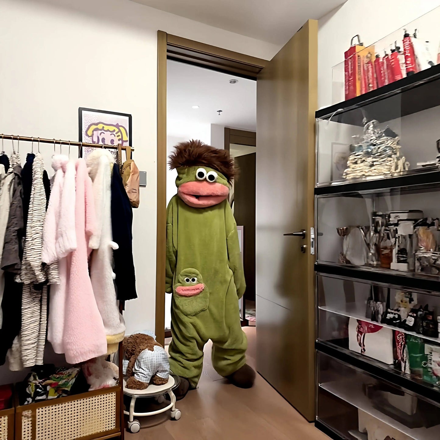 A person wearing a green monster fleece onesie pajama from zero2cart with a brown hair tuft and a pink mouth pocket.