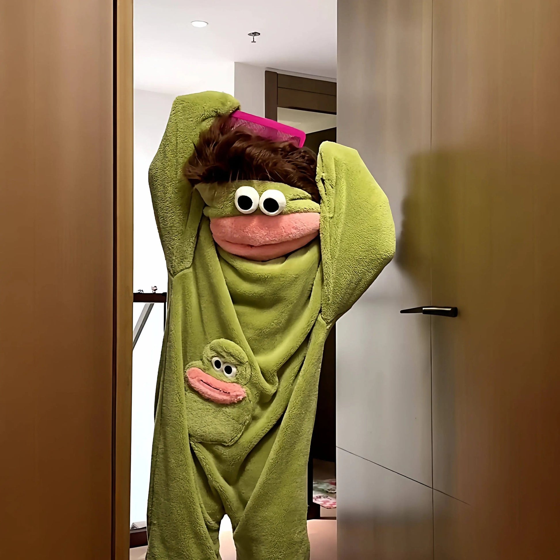 zero2cart green monster fleece onesie pajamas with a pink mouth and large eyes, worn by a person brushing their hair
