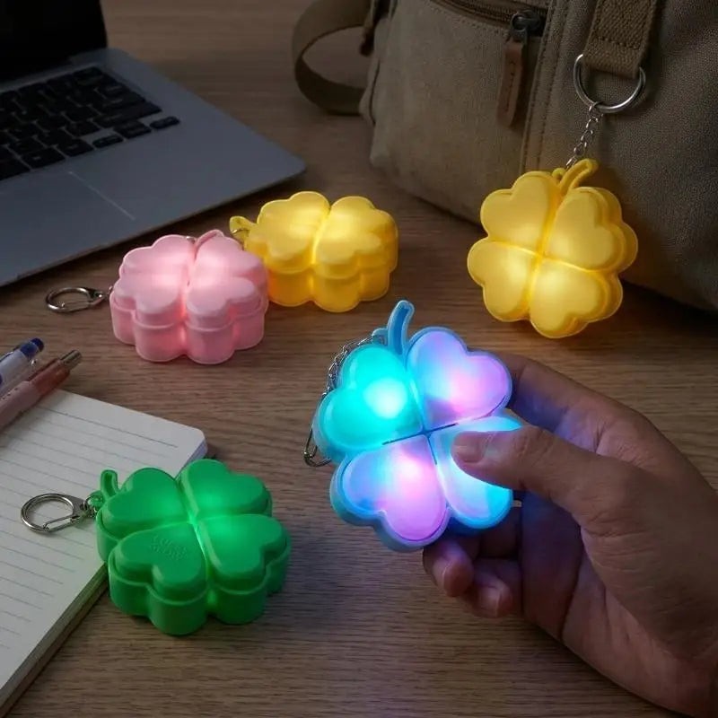 zero2cart light-up four-leaf clover fidget keychains in green, pink, yellow, and blue glowing on a desk